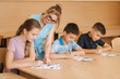 © Aleksandr - Teacher helping school kids writing test in classroom. education, elementary school, learning and people concept