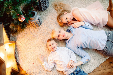 Merry Christmas and happy holidays! Cheerful mother and her cute children near the Christmas tree. Parent and two young children having fun and playing together near a Christmas tree indoors.