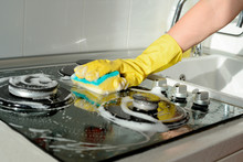 A Hand In A Yellow Rubber Glove Washes A Gas Stove On A Sunny Day. Kitchen Cleaning
