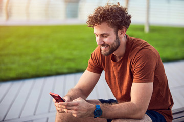 Wall Mural - Young adult man using modern cellphone in the park.