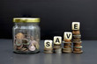 © jatupron - Saving money concept. Glass jar full of coins, stacks of coins and sign save on the black background.