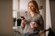 © JustLife - Young businesswoman in office. Beautiful woman drinking coffee and typing message.