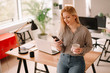 © JustLife - Young woman in office. Beautiful woman on coffee break using phone.