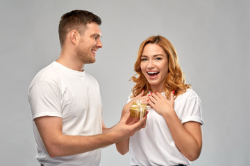 Poster - relationships, holiday and valentines day concept - happy couple in white t-shirts with christmas gift over grey background