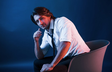 Beautiful man in glasses sits in the studio with blue neon lighting