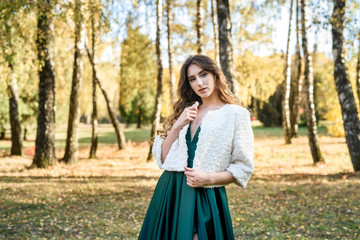 Young woman wearing fashionable green dress walking in autumn park.