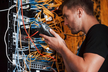 Wall Mural - Young man in uniform works with internet equipment and wires in server room