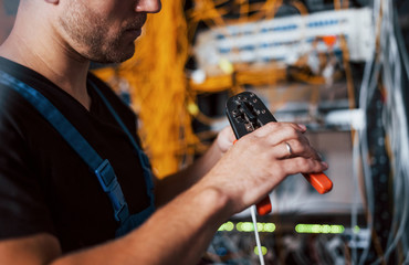 Wall Mural - Young man in uniform works with internet equipment and wires in server room