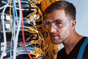Wall Mural - Young man in protective glasses works with internet equipment and wires in server room
