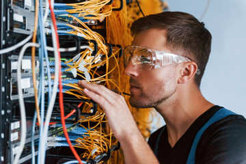 Wall Mural - Young man in protective glasses works with internet equipment and wires in server room
