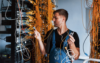 Wall Mural - Young man in uniform feels confused and looking for a solution with internet equipment and wires in server room