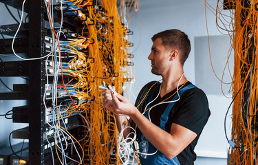 Wall Mural - Young man in uniform feels confused and looking for a solution with internet equipment and wires in server room