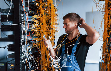 young man in uniform feels confused and looking for a solution with internet equipment and wires in 
