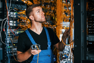 Wall Mural - Young man in uniform have a job with internet equipment and wires in server room