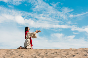 Wall Mural - jesus praying on knees in desert against sky