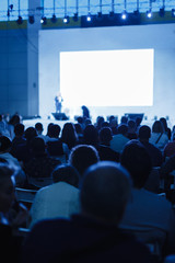 audience listens to the lecturer at the conference hall. blue tinted photo focus on unrecognizable p