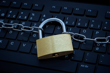 Computer keyboard protected by a metal chain and lock. Concept photo of cybercrime and internet and computer security and safety.