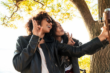 Image of two joyful african american girls taking selfie on retro camera outdoors