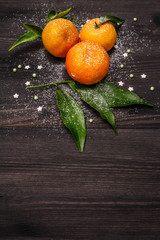 Fresh ripe tangerines with leaves and sprinkles. New Year or Christmas wooden background covered artificial snow. Festive good mood concept