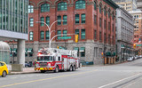 Fototapeta Nowy Jork - Fire truck responding to an alarm in the city. The fire truck is parked at an intersection in downtown surrounded by buildings. A fire fighter is getting in the vehicle.  W Cordova Street, Vancouver