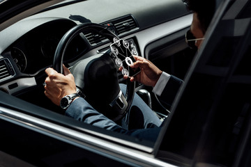 african american businessman in suit and sunglasses driving car and using smartphone with internet security icons