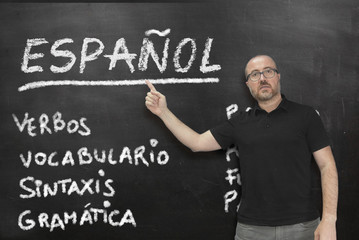 male spanish teacher pointing to some language concepts writen on a blackboard in the classroom. edu