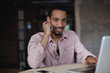 © timtimphoto - Portrait of pretty young dark skinned male freelancer with beard working out of office in coworking space, wearing earphones and looking to camera with charming smile