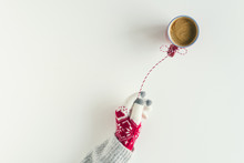 Woman Hand In A Knitted Gloves With Inflatable Air Flying Balloon Made From Cup Of Coffee Hanging On A Red White String Or Twine Tied In A Bow. White Table. Christmas Concept. Creative