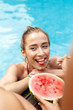 © Viktoriia - Summer Vacation. Young girl eating watermelon feeding her friend swimming in the pool looking aside playful close-up