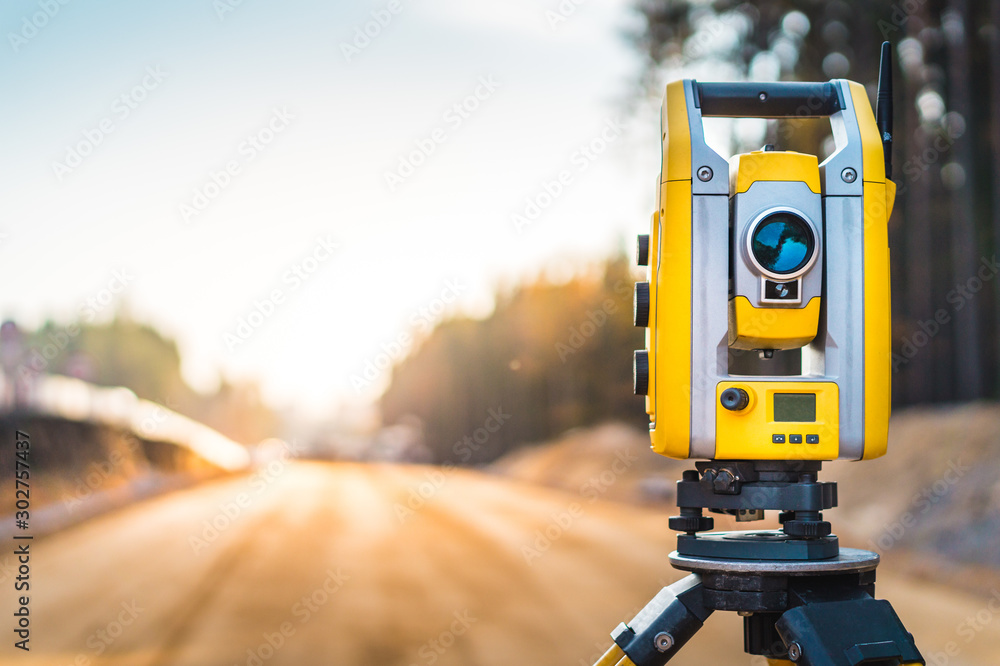 Surveyors equipment (theodolite or total positioning station) on the construction site of the road or building with construction machinery background - obrazy, fototapety, plakaty 
