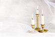 Burning candles in vintage metal candlesticks on white abstract white tulle material  background..