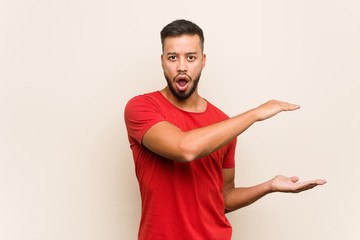 Wall Mural - Young south-asian man shocked and amazed holding a copy space between hands.