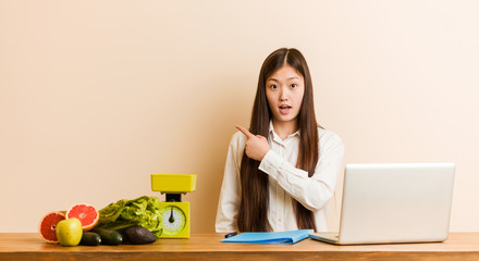 Wall Mural - Young nutritionist chinese woman working with her laptop pointing to the side