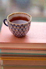 Tea in a vintage porcelain cup on stack of pastel colored books. Selective focus.