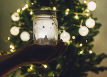 Kid Holds Christmas Lantern In Hands At Home On Lights Bokeh Background. New Year Celebration Concept, Festive Mood