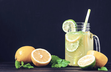 Lemonade drink of soda water, citrus and mint on the dark background. Cocktail glass with handle and straw, sliced lemon and lime, front view