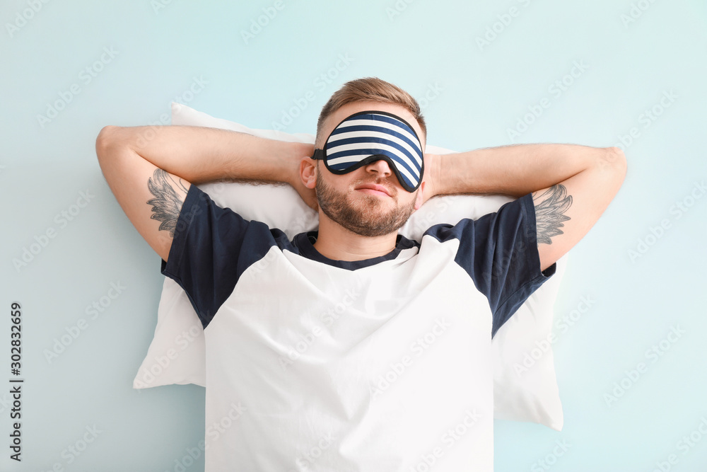 Sleeping young man with pillow on color background