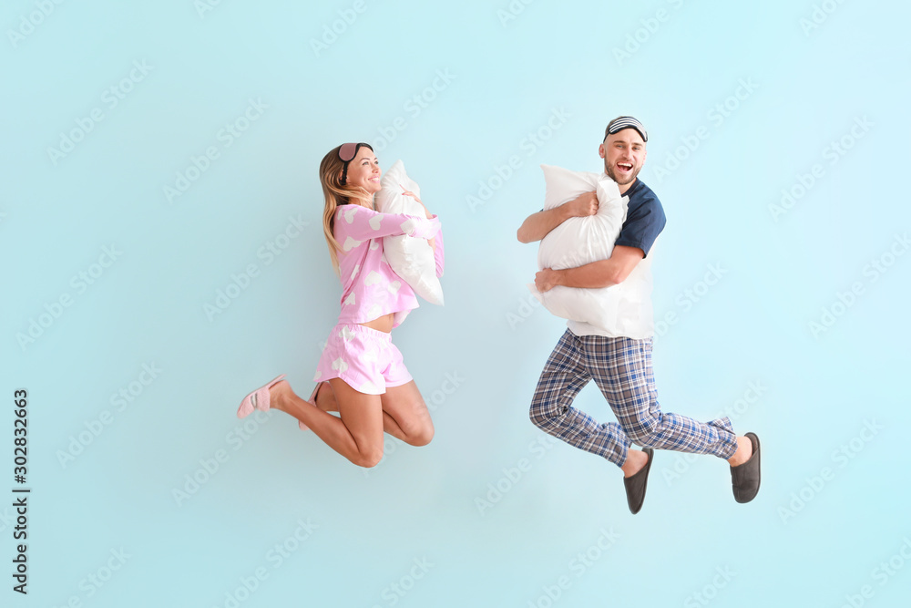 Jumping young couple with pillows on color background