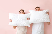 Young couple with pillows on color background