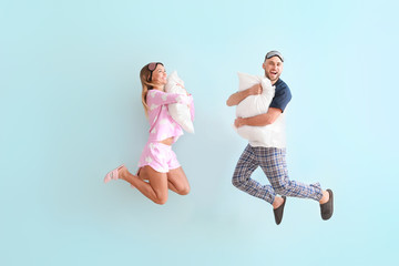 Jumping young couple with pillows on color background