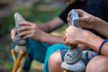A Man Makes Balancing Stones In The Forest, A Selective Focus Close Up On Hands Holding Stones And Try To Find A Balance On Wooden Tripod