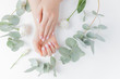 Stylish plain female hand manicure gel polish on white flower background eucalyptus, top view. Concept natural organic skin care