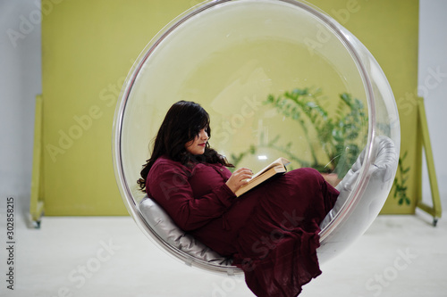 Cuadros en Lienzo Attractive south asian woman in deep red gown dress posed at studio and read a book at rocking chair ball