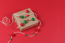 Craft Gift Box Decorated With Red And Green Beads On Red Background. Christmas Colours, Top View, Minimal Style, Copy Space