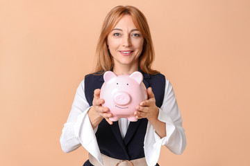 Mature woman with piggy bank on color background