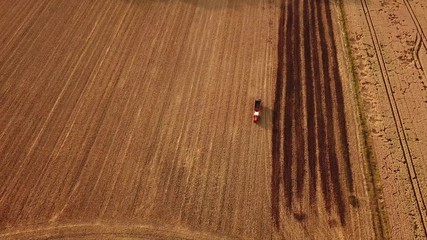 Wall Mural - Aerial tracking shot of red tractor driving on a field in summer
