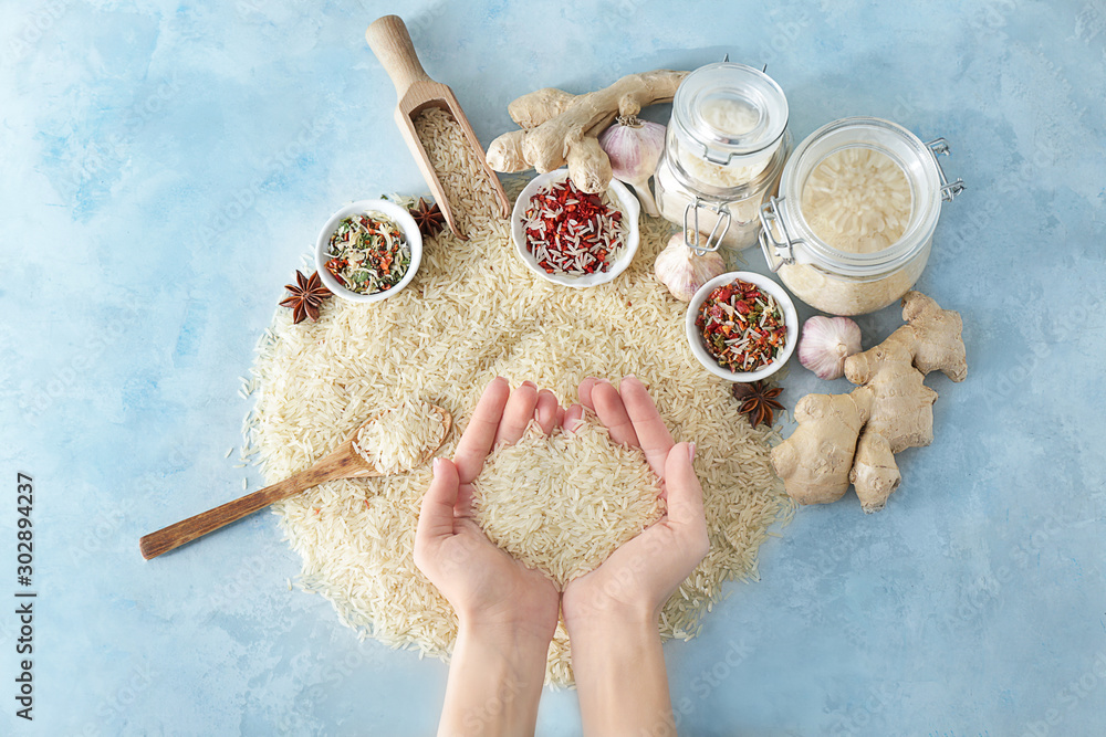 Female hands with raw rice with spices on color background