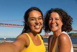 Fototapeta Do akwarium - Happy women smiling at camera. Portrait of beautiful cheerful multiethnic women standing together near river and smiling at camera. Emotion concept