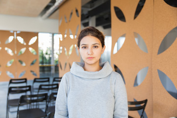 Wall Mural - Serious female student posing in auditorium. Closeup of young Caucasian woman standing in training room, looking at camera. Female portrait concept