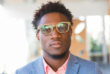 Serious Trendy Guy Posing Indoors. Closeup Of Young African American Man Wearing Stylish Glasses, Bright Shirt And Jacket, Looking At Camera. Fashion Or Male Portrait Concept
